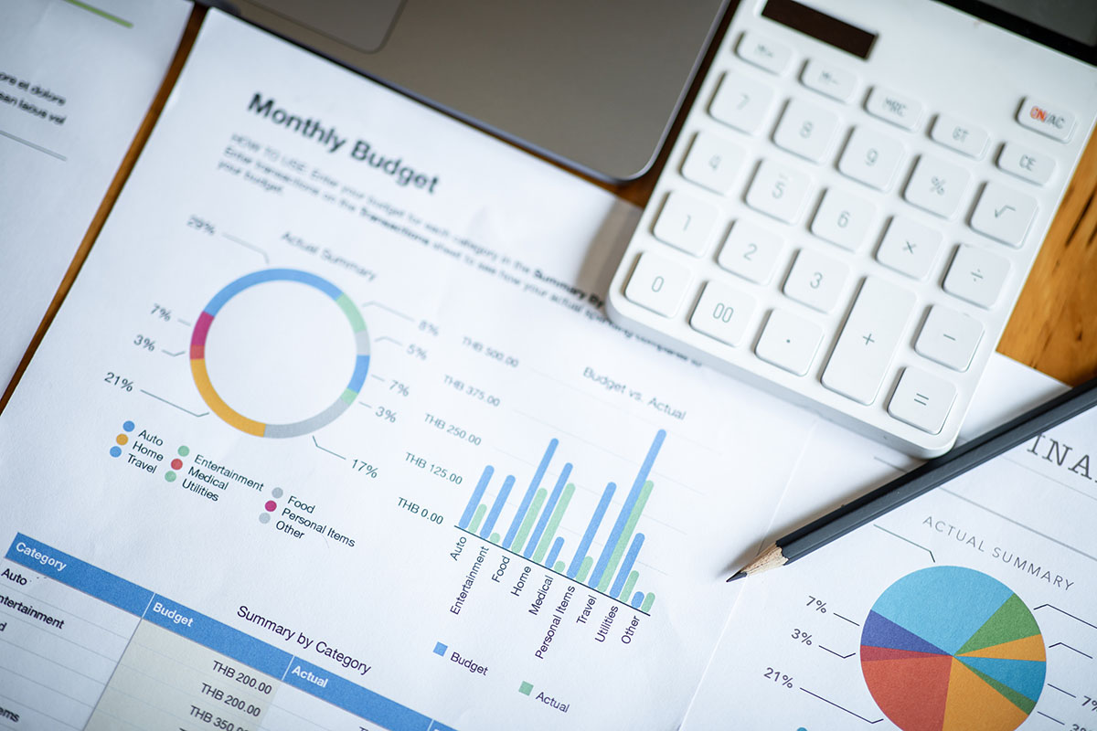 Printed monthly budget reports with donut, bar and pie charts beside a white calculator and a pencil on a wooden desk