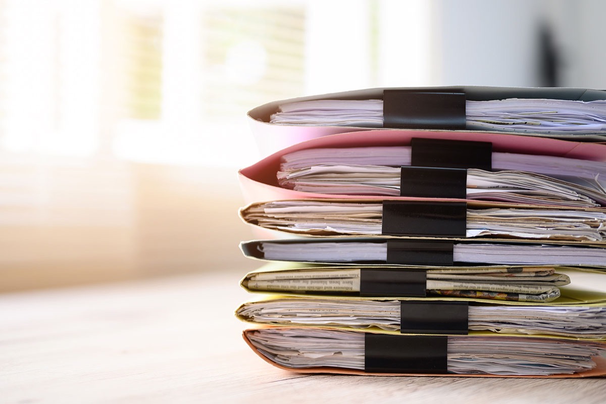 Stack of clipped paper files and folders on an office desk, a visual reminder of the manual invoice records that structured e-invoicing is replacing